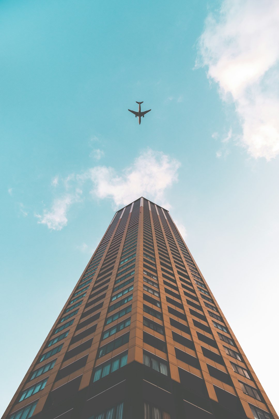 bottom-view-shot-of-airplane-flying-above-high-rise-building-kxcjxxgsv9i